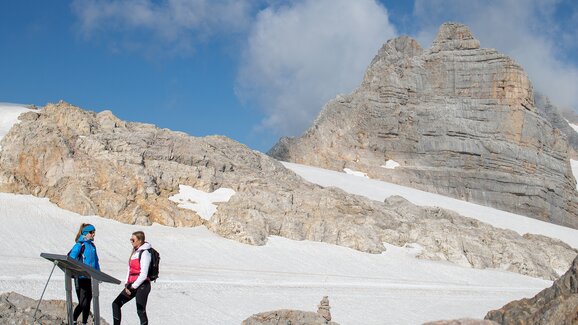 Zwei Frauen in Wanderkleidung stehen an einer Infotafel auf einem Gletscher, umgeben von schroffen Felsen und Schneefeldern. | © Birgit Walcher