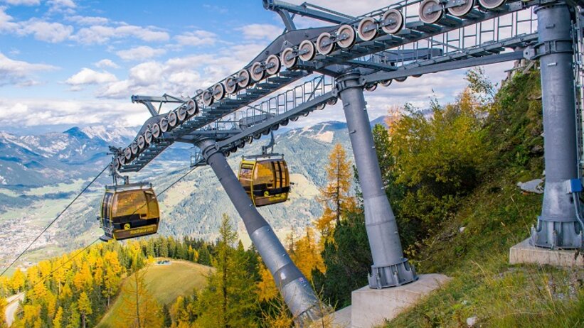 Gelbe Gondeln der Hochwurzenbahn fahren durch herbstlich gefärbten Wald mit Blick auf das alpine Tal. | © Alexander Klünsner