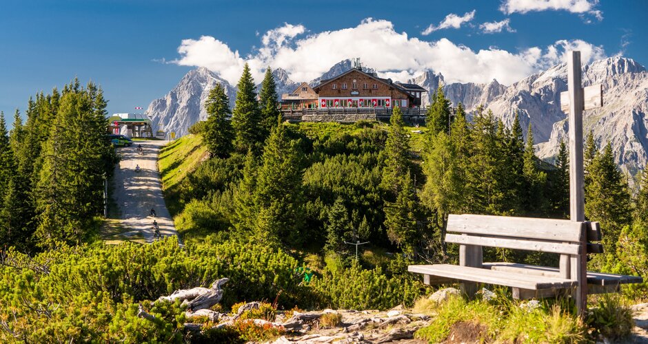 Almhütte auf der Hochwurzen mit Terrasse, umgeben von Wald, Bergen und klarer Sommerluft unter blauem Himmel. | © Christine Höflehner