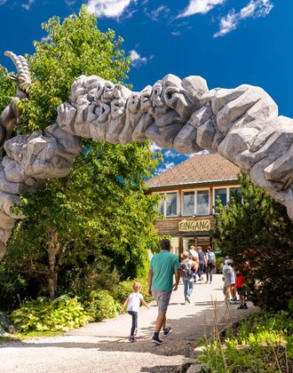 Besucher gehen durch das steinerne Eingangstor zum Wilden Berg in Mautern mit Tierfiguren. | © Christine Höflehner