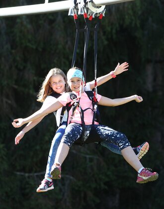 Two girls hang side by side on the Rittisberg Flyline, smiling with arms stretched out as they glide smoothly through the air. | © Erlebnis Rittisberg