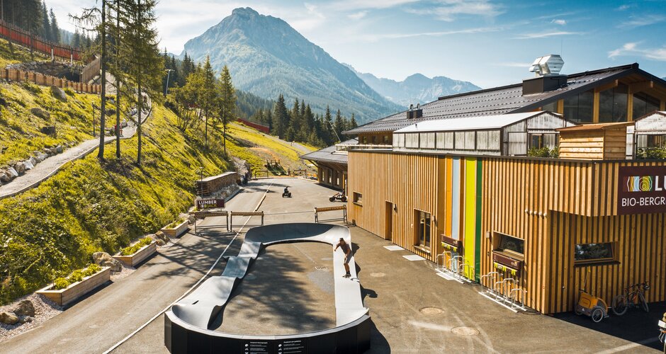 Skater on a pumptrack in front of the wooden bio-mountain restaurant in alpine surroundings. | © Shuttleberg
