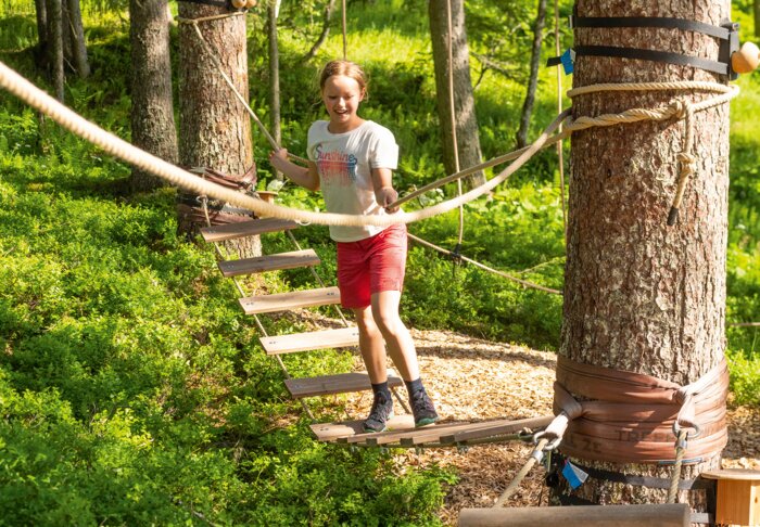 Mädchen überquert Hängebrücke im Waldseilgarten bei sonnigem Wetter. | © Shuttleberg