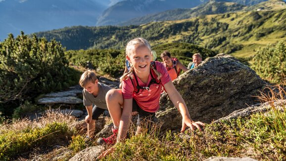 Mädchen klettert lachend über Felsen, gefolgt von Familie beim Sommerwandern im Gebirge bei Flachau im Salzburger Land. | © TVB Flachau, Ulrich Grill