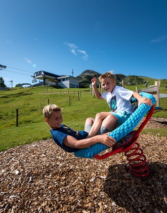 Two laughing kids swing on rope seat near Gamskogelbahn Zauchensee during summer vacation. | © Zauchensee Liftgesellschaft