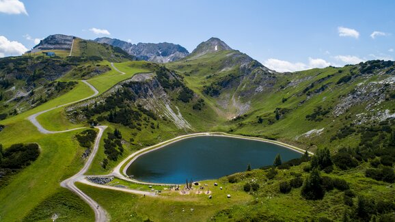 Speichersee mit umlaufendem Panoramaweg, Spielstation und Almen inmitten der grünen Berglandschaft Zauchensees