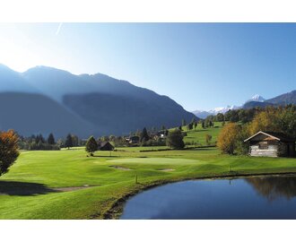 Idyllischer Blick auf den Golfclub Goldegg mit Teich, Almhütte, grünen Fairways und verschneiten Bergen im Hintergrund. | © Golfclub Goldegg