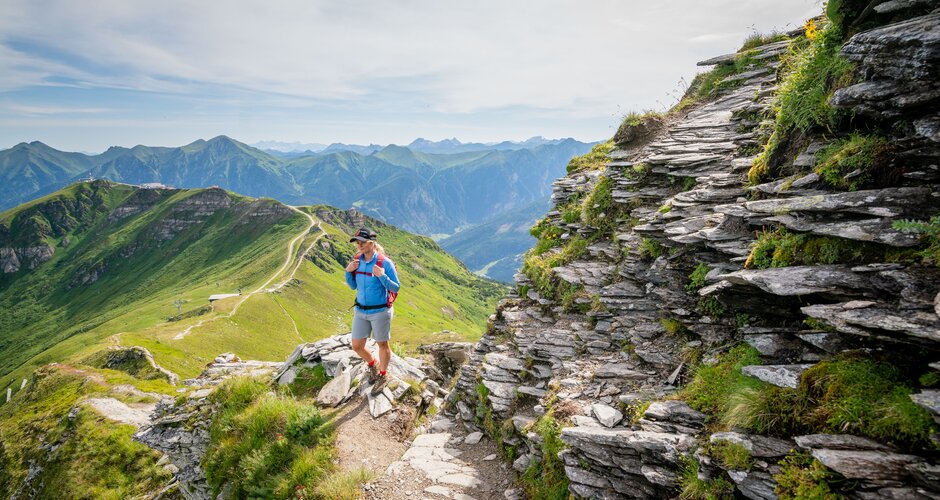 Hiker on narrow mountain path among rocks with wide view across green Gastein alpine landscape | © Gasteinertal Tourismus GmbH, Oberschneider