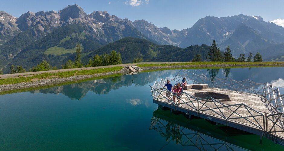 Family on wooden platform at Prinzensee in Maria Alm, clear lake water and Hochkönig mountains in background | © Roland Haschka