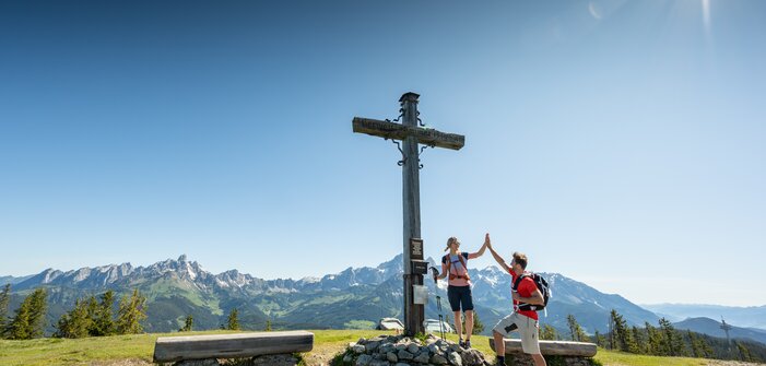 Two people stand on a plateau by a summit cross and give each other a high five | © Tourismusverband Radstadt/Lorenz Masser