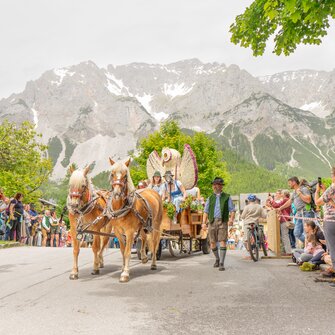 Horse parade with decorated wagon at Ramsau spring festival, crowd on roadside, Dachstein mountain in the background | © Simone Raninger