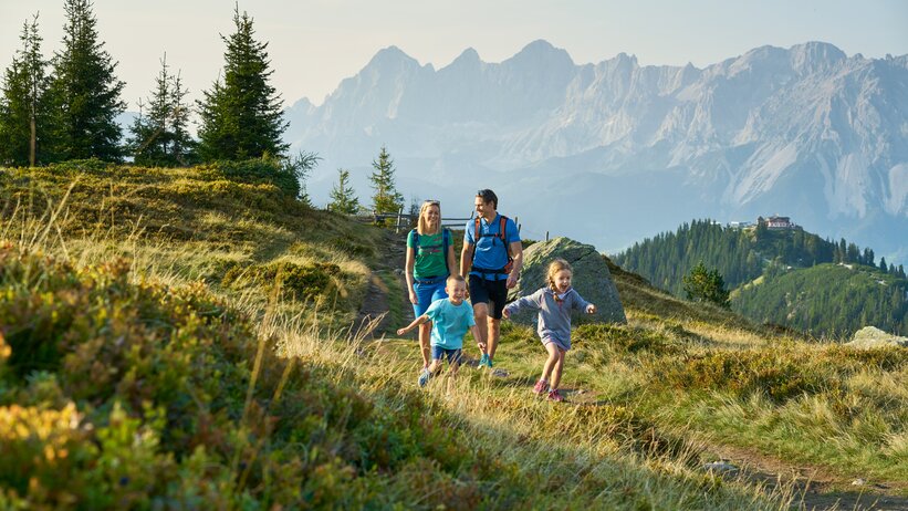 Familie wandert bei Sonnenschein über Almwiesen mit Blick auf das Dachsteinmassiv in Schladming-Dachstein | © Peter Burgstaller