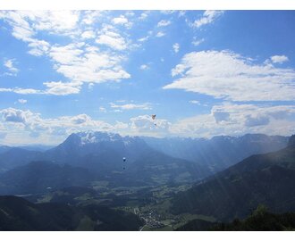 Mehrere Gleitschirmflieger schweben hoch über einer grünen Alpenlandschaft mit Bergen und Tälern unter blauem Himmel. | © Flugschule Aufwind