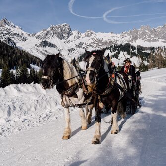 A horse-drawn sleigh with two horses glides through the snowy mountain landscape. | © Chris Perkles