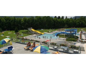 Sommerliches Schwimmbad mit Rutschen, Pool und grüner Liegewiese inmitten der Natur.