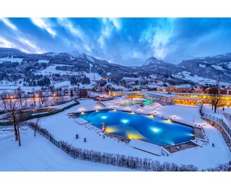 Die Alpentherme Gastein mit beleuchtetem Außenbecken in verschneiter Winterlandschaft. | © Gerhard Wolkersdorfer