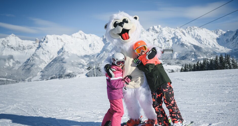 Two children with ski equipment hug a person in polar bear costume who is also on skis | © Christian Schartner