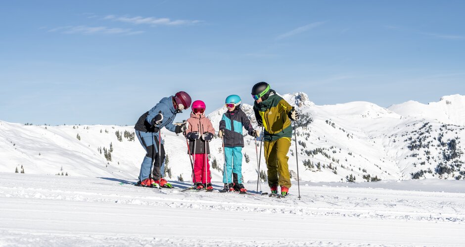Vierköpfige Skifamilie steht nebeneinander auf breiter Skipiste in Dorfgastein mit Blick auf verschneite Berglandschaft | © Dorfgasteiner Bergbahnen