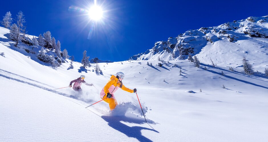 Two skiers glide through deep powder snow under bright sun at Hauser Kaibling. | © Hauser Kaibling