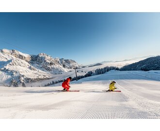 Two skiers at sunrise on freshly groomed slope in Mühlbach with alpine backdrop | © Hochkönig Tourismus GmbH