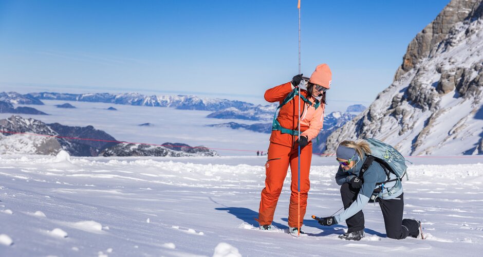 Two women practice avalanche rescue with probe and transceiver in glacier snow. | © René Eduard Perhab