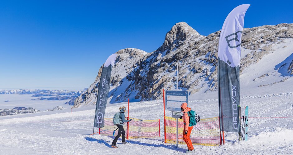 Two winter sports enthusiasts at a training area with flags, fence and mountain backdrop on Dachstein Glacier. | © René Eduard Perhab