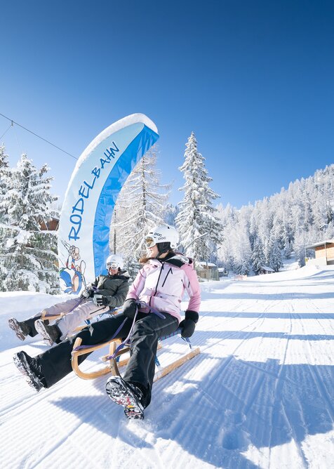 Zwei Personen rodeln bei Sonnenschein auf präparierter Winterbahn in Galsterberg. | © Josh Absenger