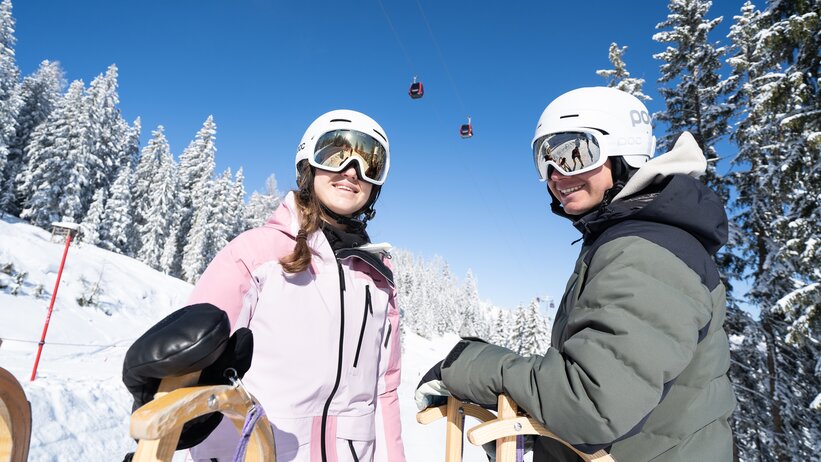 Zwei Personen mit Helmen und Schlitten im Schnee bei Sonnenschein in Galsterberg. | © Josh Absenger