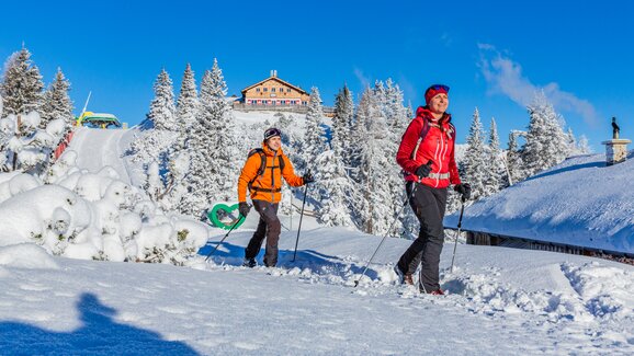 Two hikers with snowshoes walking on snowy trail with mountain panorama. | © René Eduard Perhab