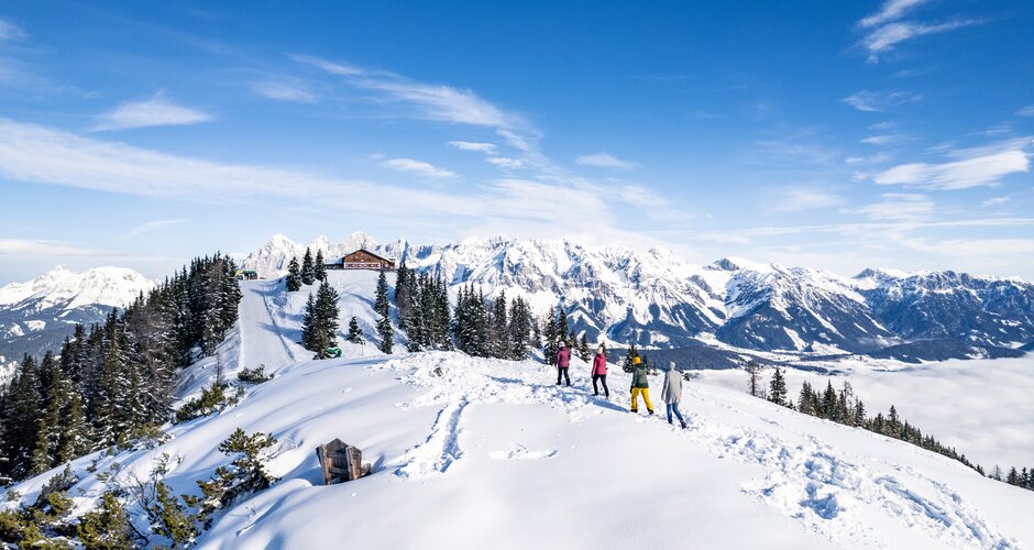 Winter hikers with snow-covered mountains and blue sky in the background. | © Gerald Oberreiter