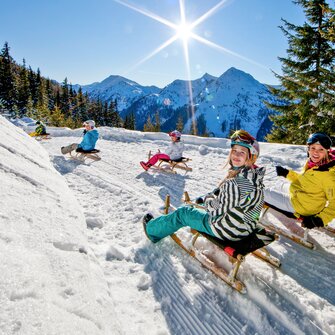 Five tobogganers on snowy run in Hochwurzen with sunshine and mountain view | © Tom Lamm