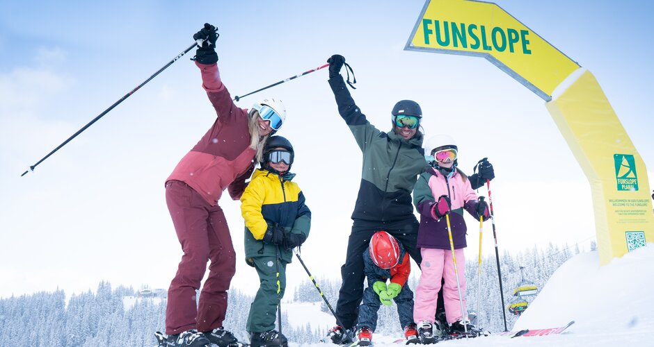Happy family on skis and wearing ski suits stands at the start of a fun slope | © Josh Absenger