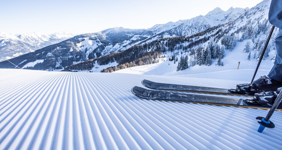 Skis on a freshly groomed slope with a snowy alpine landscape in the background. | © Mirja Geh