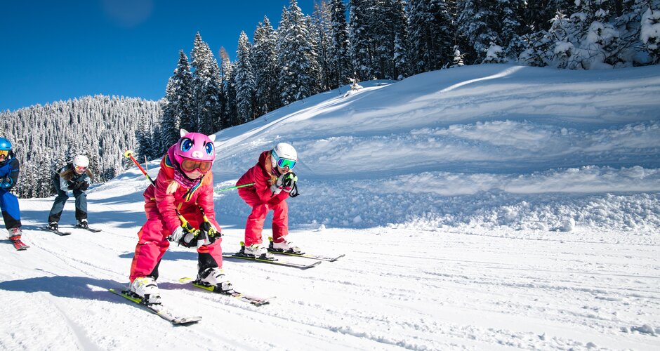 Two children crouch down on their skis and ski along a tow path with their parents following right behind them | © Salzburger Sportwelt, Christian Schartner