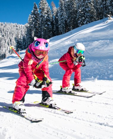 Two children crouch down on their skis and ski along a tow path with their parents following right behind them | © Salzburger Sportwelt, Christian Schartner