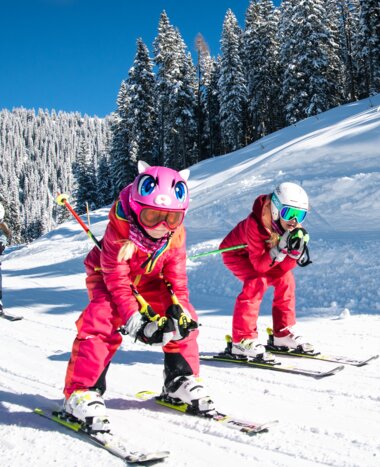 Two children crouch down on their skis and ski along a tow path with their parents following right behind them | © Salzburger Sportwelt, Christian Schartner