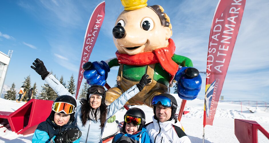 Family sits before hedgehog statue with crown standing in the snow
