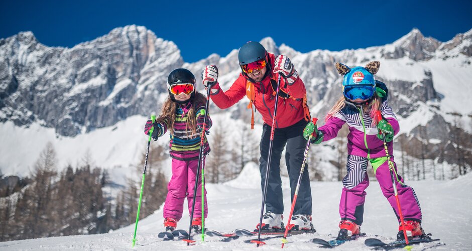Family with two children skiing in front of a snow-covered mountain backdrop. | © Christine Höflehner