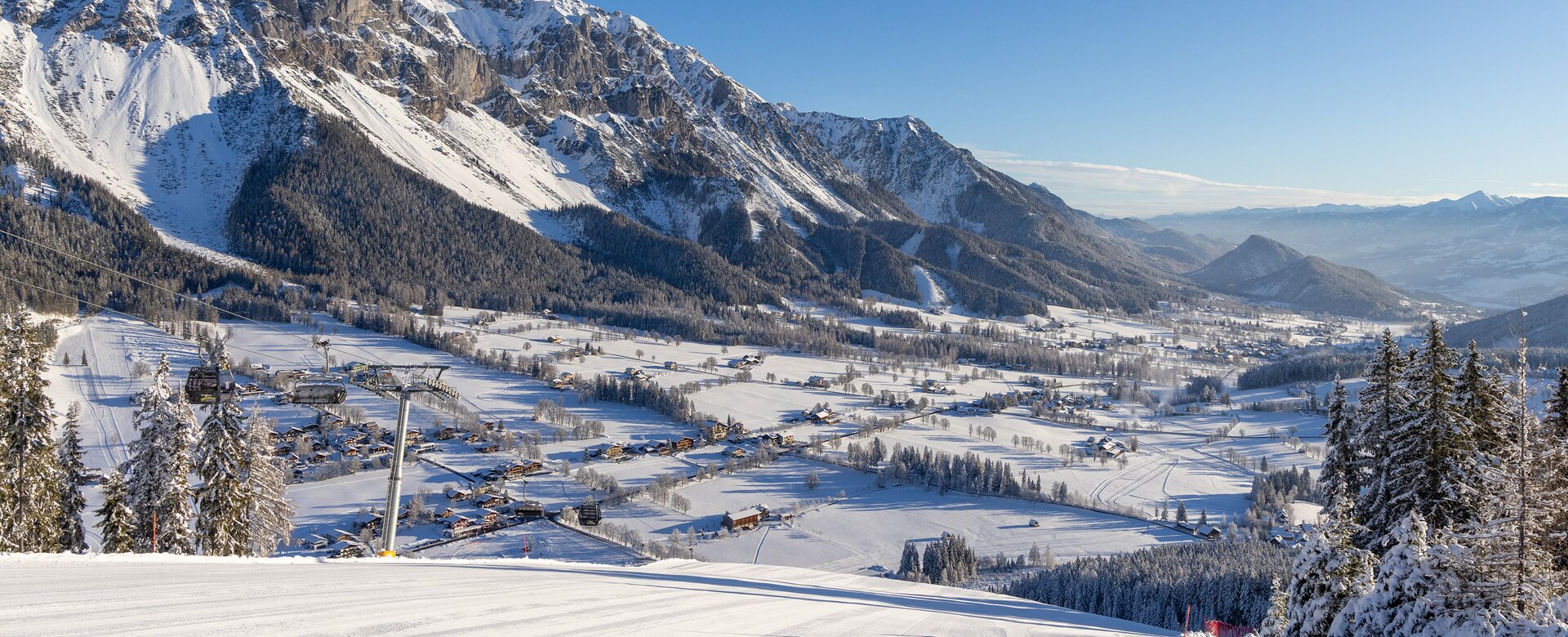 Blick von präparierter Skipiste auf verschneites Ennstal und markante Bergkulisse.