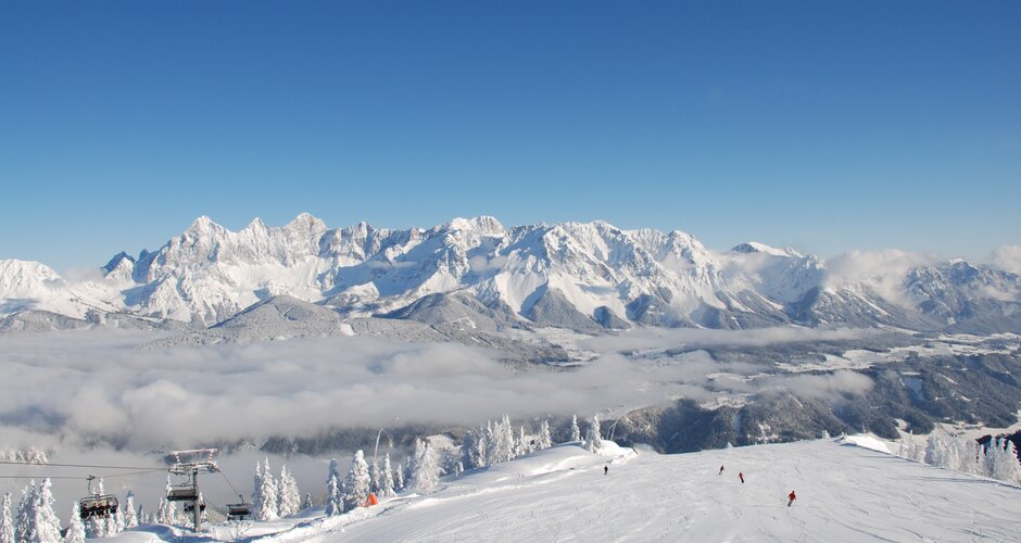 View of snowy slope, skiers, and impressive mountain panorama in the background.