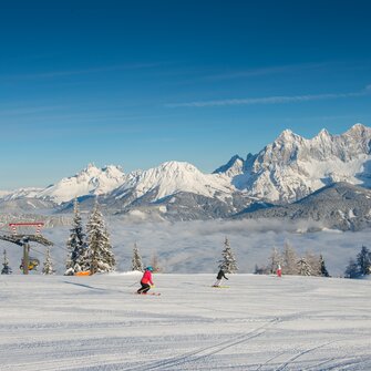 Two skiers on groomed slope at Reiteralm, with snow-covered Dachstein mountains behind. | © Lorenz Masser