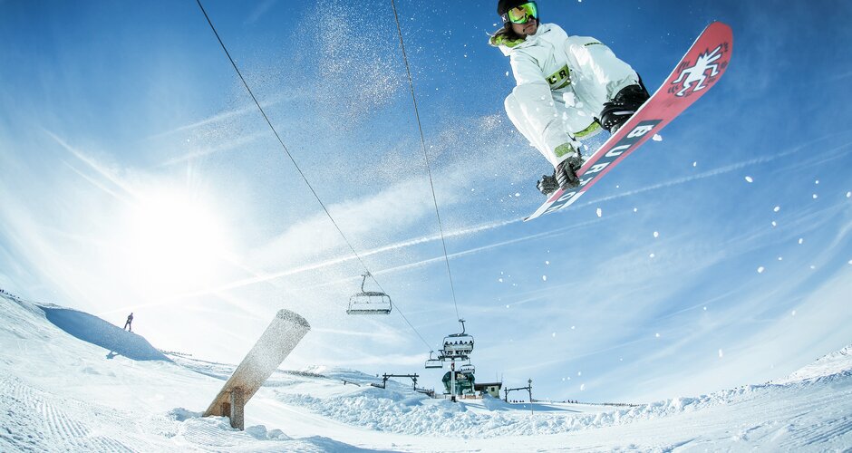 Snowboarder springt hoch in The Stash Park, mit Sonnenschein, Schnee, Liften und blauem Himmel | © Shuttleberg