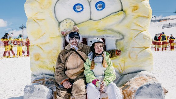 A person in a bunny costume and a girl in a ski suit sit on a statue made of snow that looks like Spongebob. | © Markus Rohrbacher