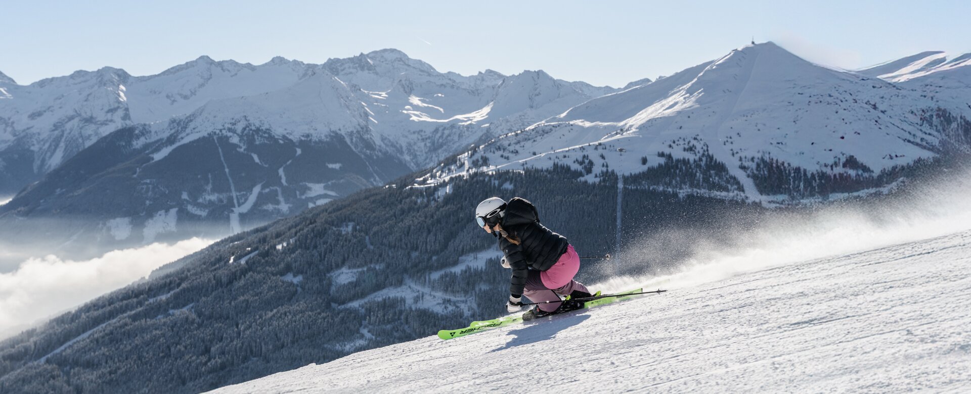 Skifahrerin in Kurve auf Piste mit Blick auf verschneite Wälder und Berge | © Simon Hutter