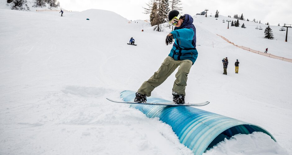 Snowboarder at Betterpark Alpendorf on rail slide, snowy slope and spectators | © Gert Perauer