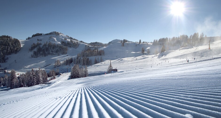 Perfectly groomed ski slopes at Alpendorf ski area with sun, snow and mountains