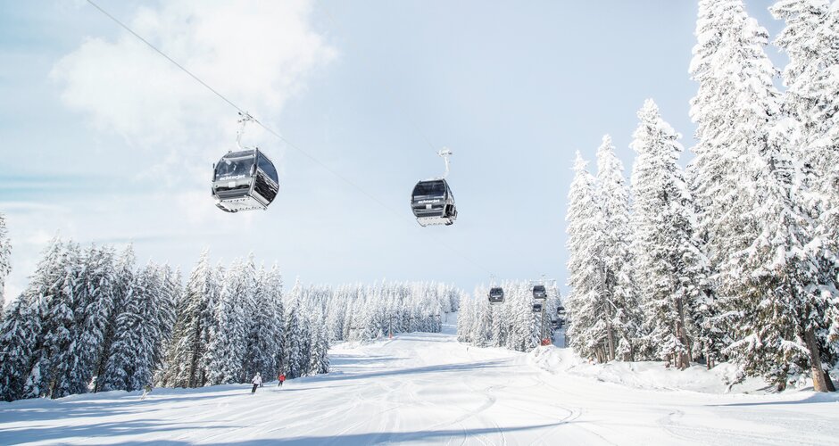 Achterjet Kabinenbahn Flachau mit Gondeln, verschneiten Tannen und präparierter Piste | © Snow Space Salzburg