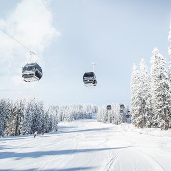 Achterjet Kabinenbahn Flachau mit Gondeln, verschneiten Tannen und präparierter Piste | © Snow Space Salzburg