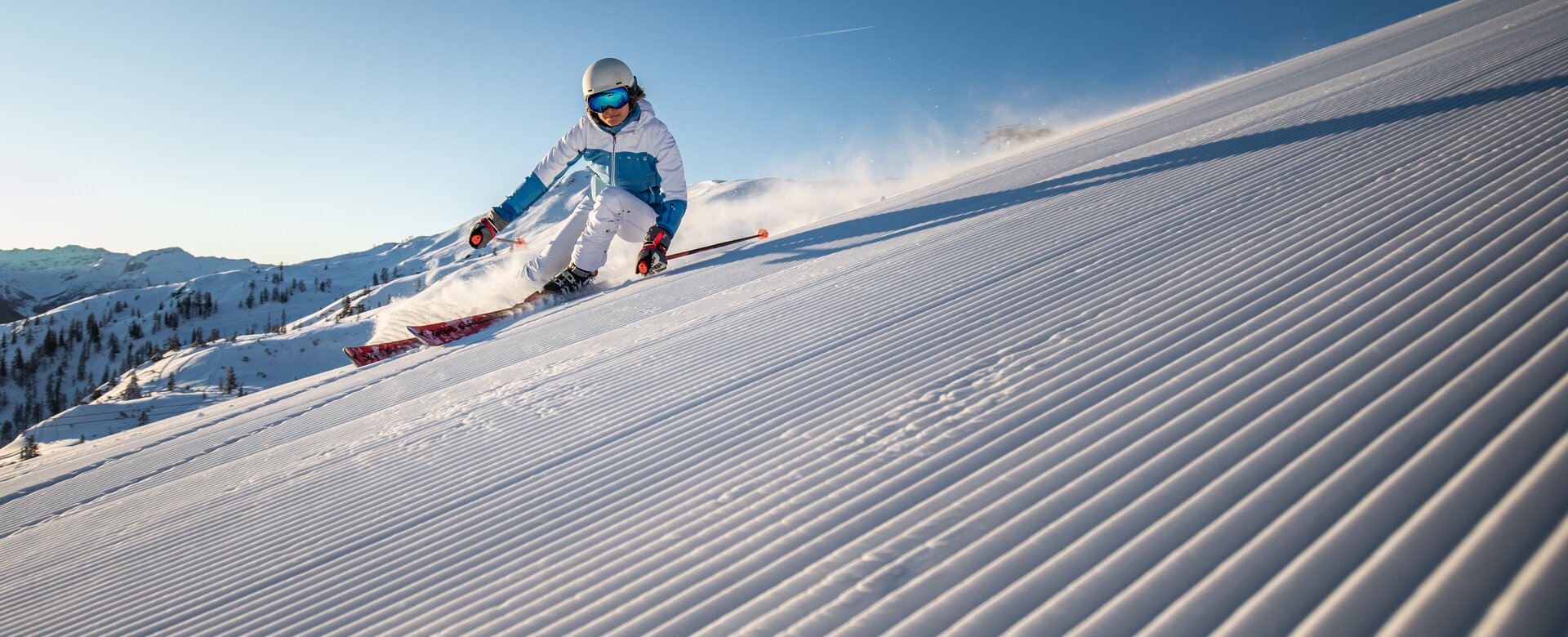 Skifahrerin in weißem Outfit auf frisch präparierter Piste bei Sonnenaufgang | © Michael Grössinger Fotografie