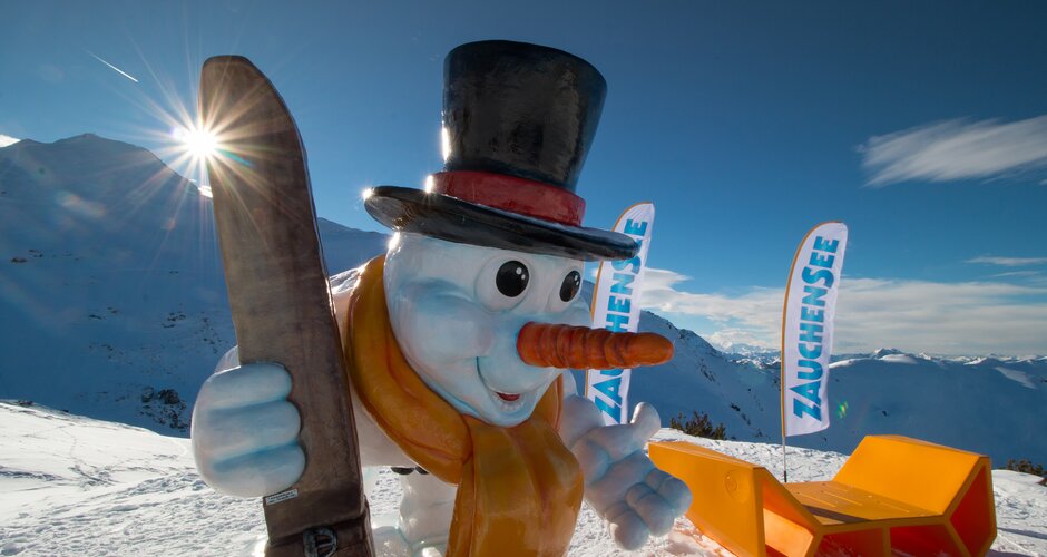 A colorful snowman with ski goggles and wooden ski, mountains and Zauchensee flags